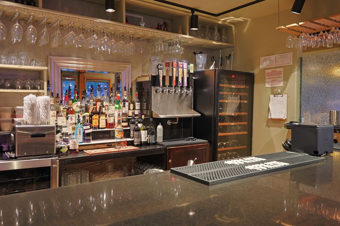 Bar back with hanging glassware, spirit bottles, draft taps and a wine fridge