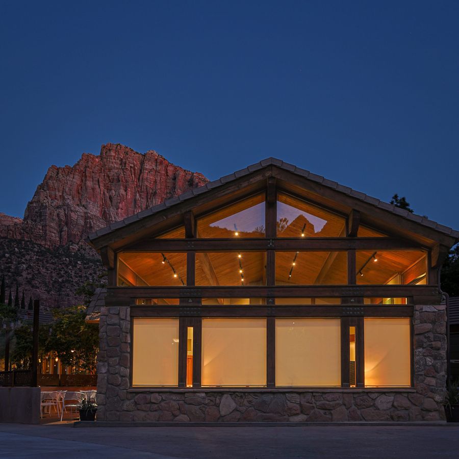Timber and stone lodge glowing at blue hour beneath red canyon cliffs