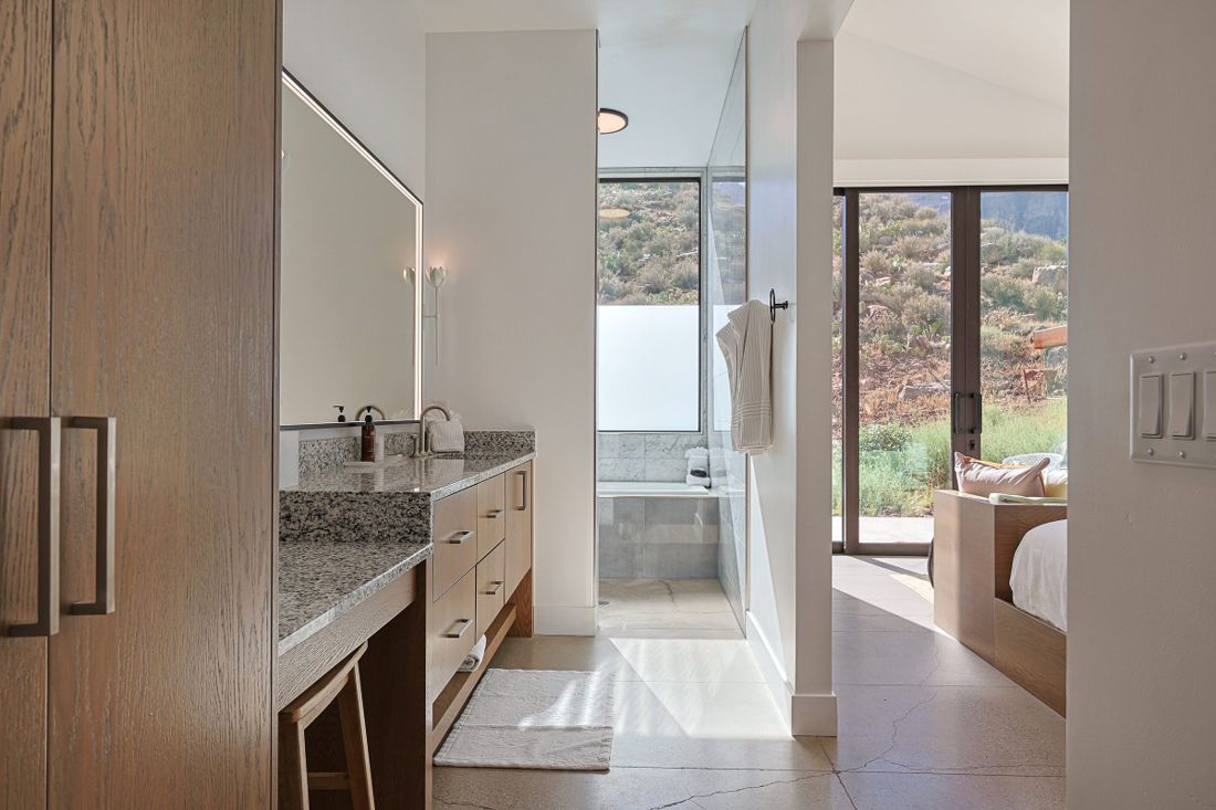 Suite vanity and walk-in shower opening onto a bedroom with desert hillside views