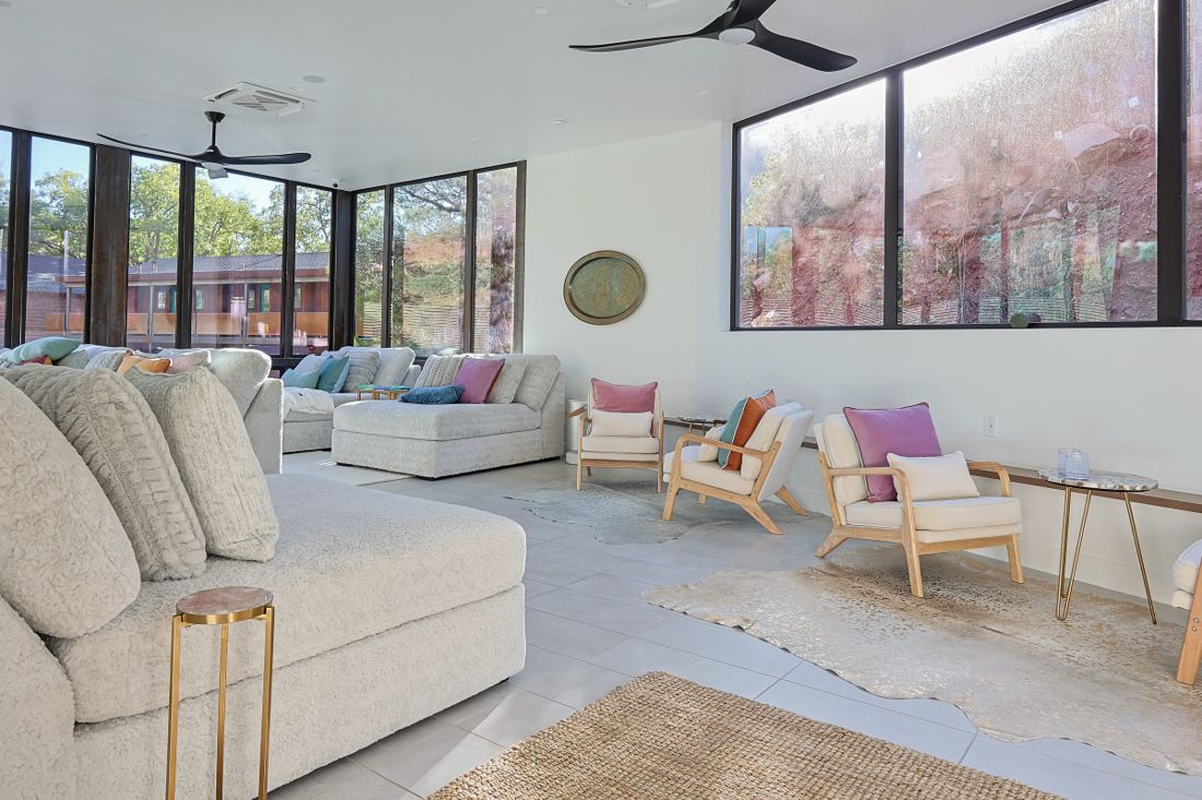 Airy sunroom lounge with sectional sofas, armchairs and woven rugs beside floor-to-ceiling windows