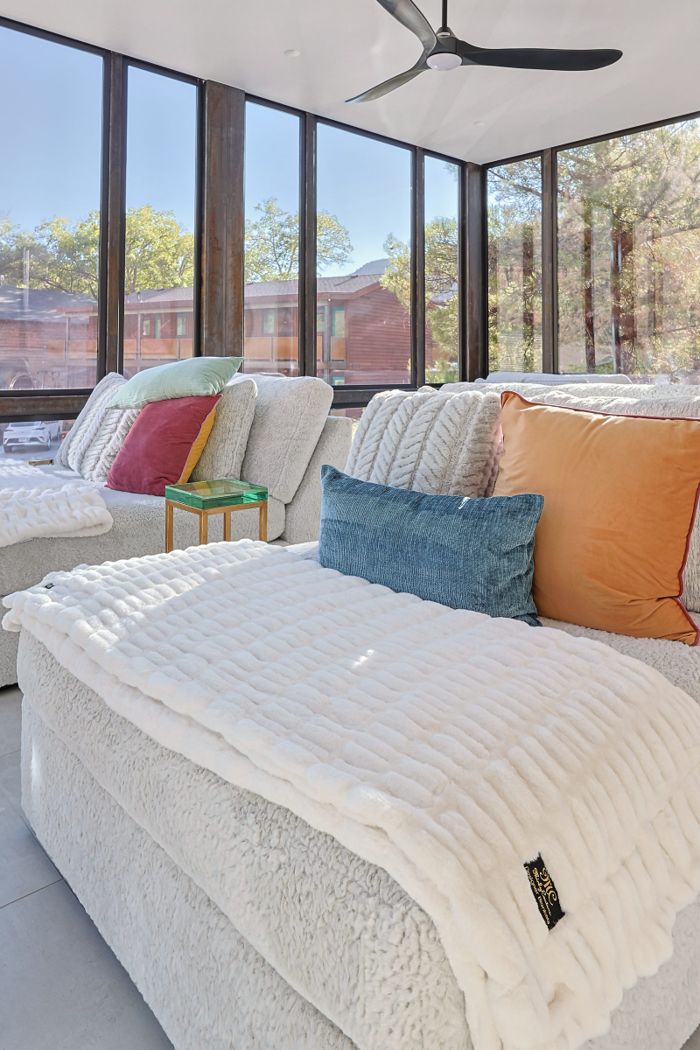 Faux fur throw, cushions and warm textiles layered across a sunlit lounge sofa