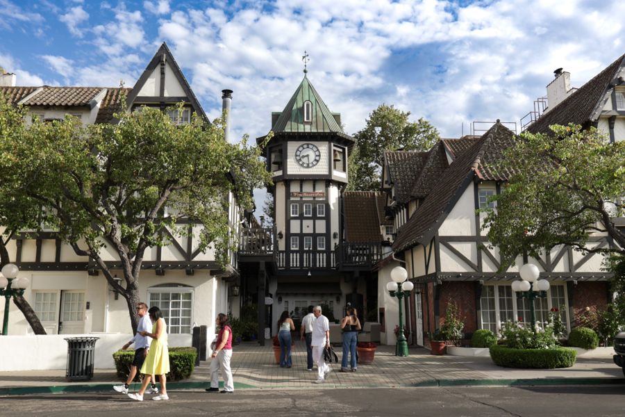 Half-timbered village square with a clock tower and visitors walking in afternoon sun